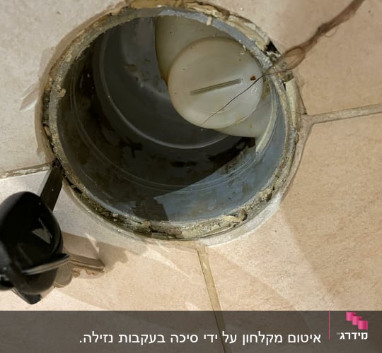 פתח ניקוז עם מכסה פלסטיק ומפתח על הרצפה